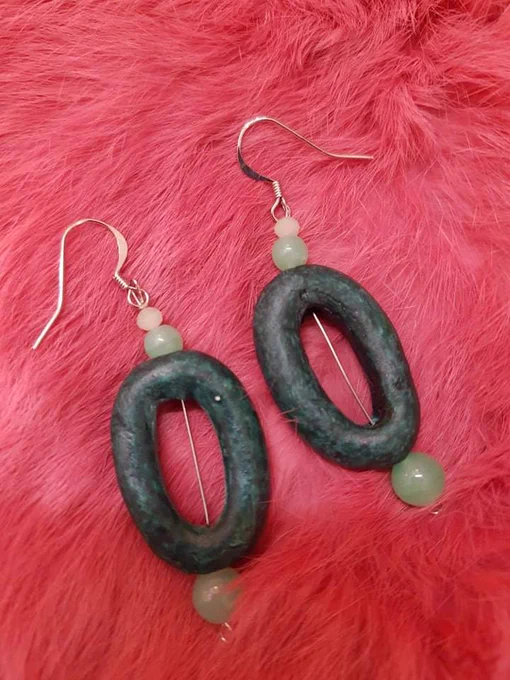 earrings on dyed pink rabbit fur. the earrings are large oval hand carved wooden beads that are a dark green. they have real jade beads, and light green faceted crystals.