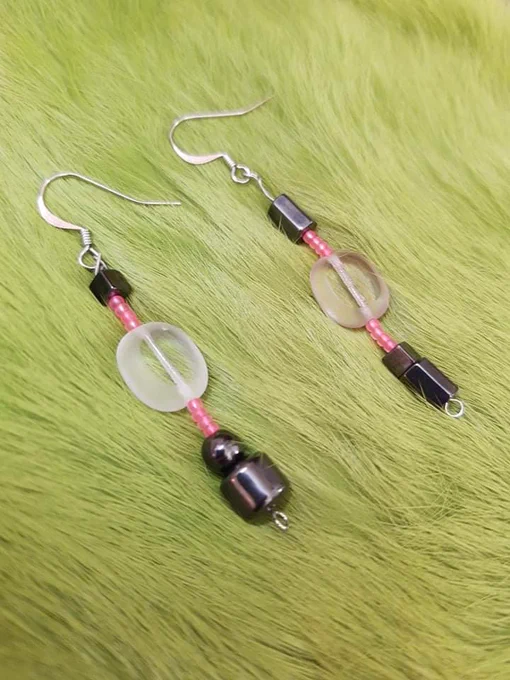 pair of earrings on green dyed rabbit fur. the earrings are mismatch hematite with a large clear almost beach glass looking bead, with hot pink seed beads in between.
