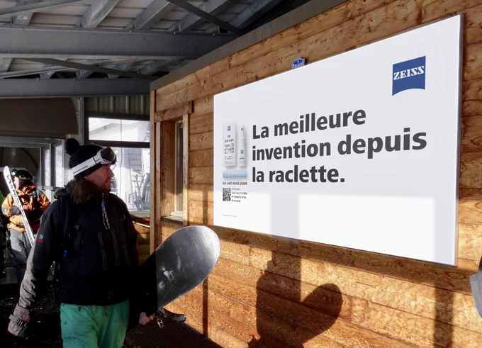 Dans une station de ski, une publicité pour le kit antibuée Zeiss qui dit : La meilleure invention depuis la raclette.