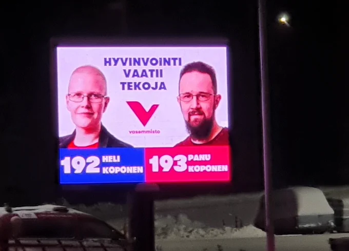 Vasemmiston aluevaalivalomainos Kouvolassa. "Hyvinvointi vaatii tekoja" ja Heli Koposen 192 ja Panu Koposen 193 kasvot.
