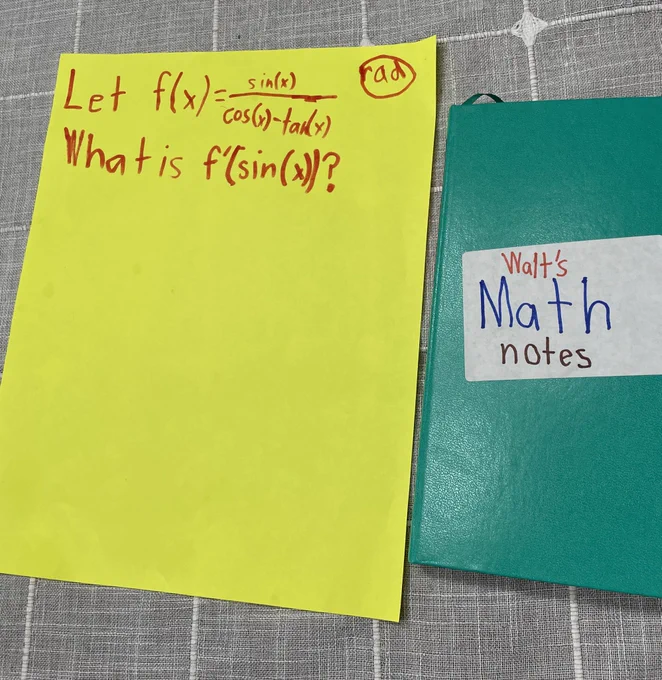 A piece of yellow paper with child handwriting with the following equation in marker: Let f(x)=sin(x)/cos(x)-tan(x). What is f’(sin(x))? (Expressed in radians). 
To the right of the paper is a teal notebook. The cover has a handwritten, in child handwriting, label that says “Walt’s Math notes”