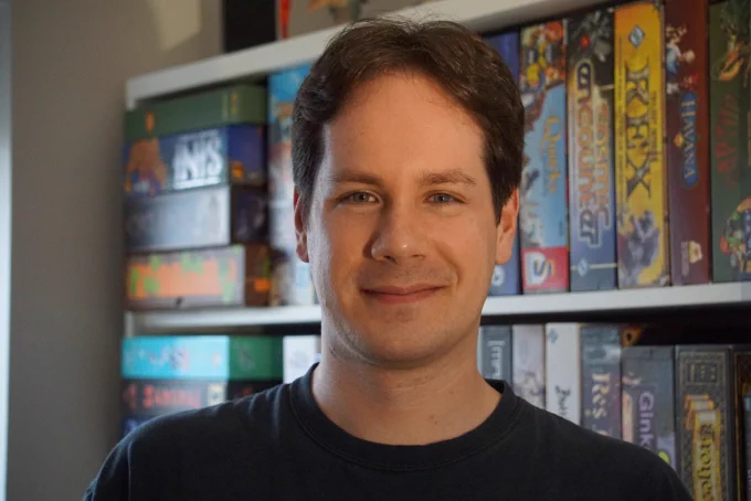 A portrait of Manuel Correia with boardgames on the background.
