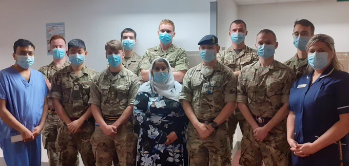 Army personnel and NHS staff stand in a row, all wearing blue surgical masks.