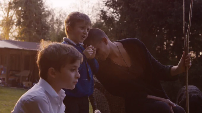 [Image description: A graphic contains a film still from 'A Space In Time' showing Klara, a white women in about her 40s, leaning on Theo, a young white boy and Oskar in the shot, a young white boy.] 