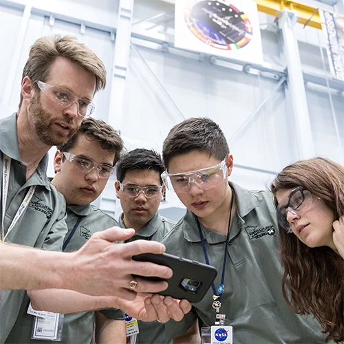 A team of students and their teacher look at a mobile phone during a competition
