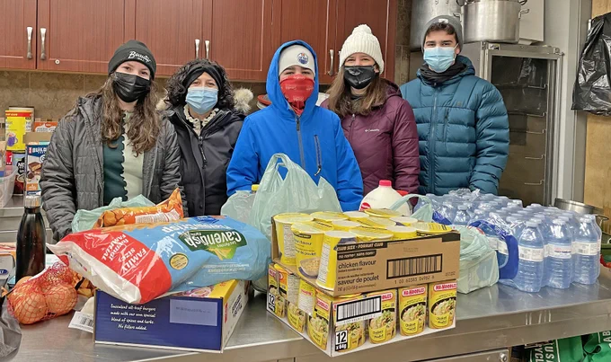 Five people stand behind donated food and water bottles.