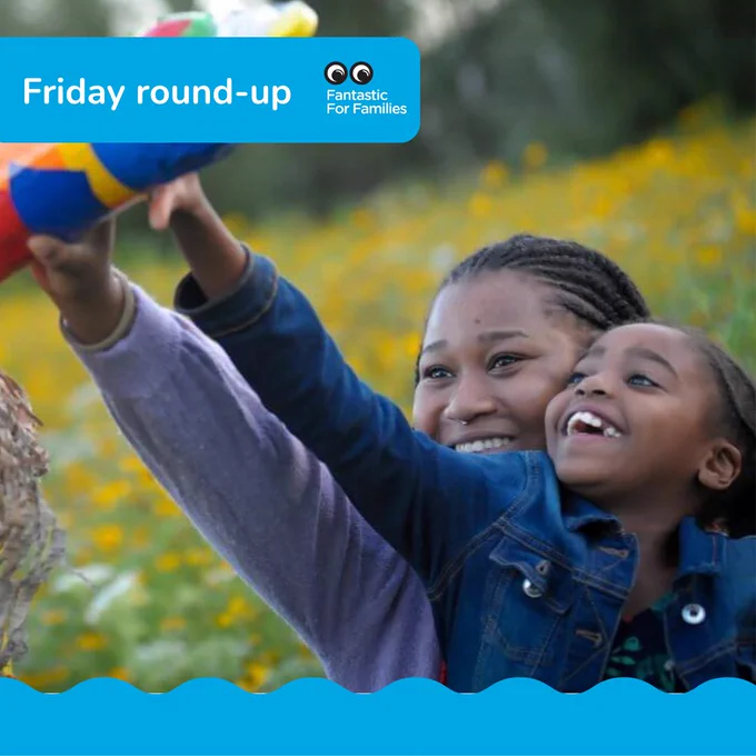 A black woman and child, wearing blue jackets, on a meadow, holding up a colourful cardboard rocket over their heads