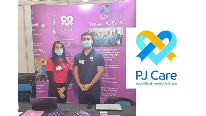 Two people wearing face masks standing in front of a banner for PJ Care at a jobs fair. Includes PJ Care's logo