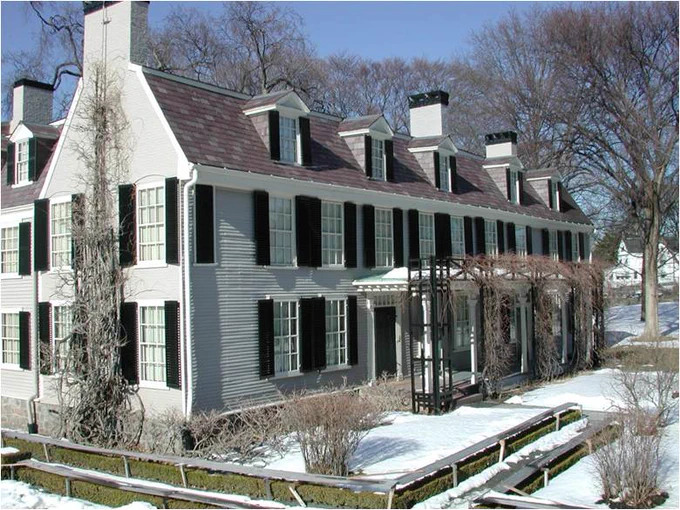 Large grey house with black shutters covered in snow.
