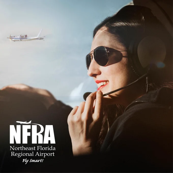 Photograph of female pilot with headphones with a microphone on looking out an aircraft windshield to view a blue sky and aircraft in flight. Logo of the Northeast Florida Regional Airport is in the lower left hand corner of the image.