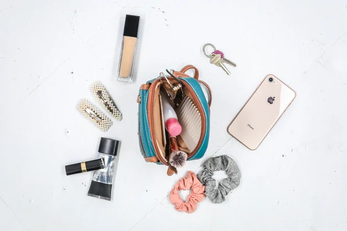 Our Micro Everest Crossbody Bag is open on the table and surrounded by all of our essentials that we carry within it.