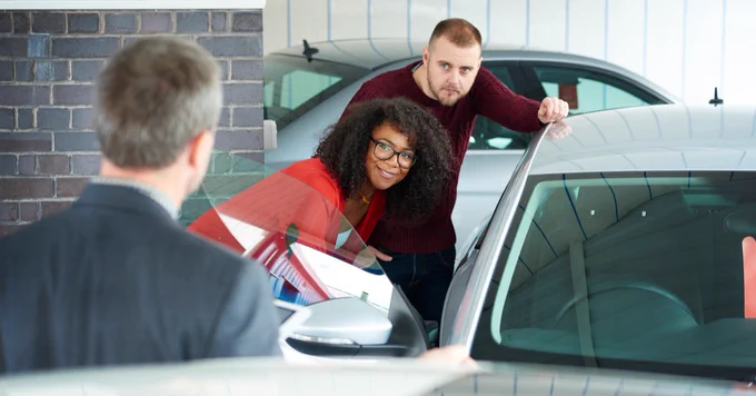 (alt="A couple looking at a car in a car show room")