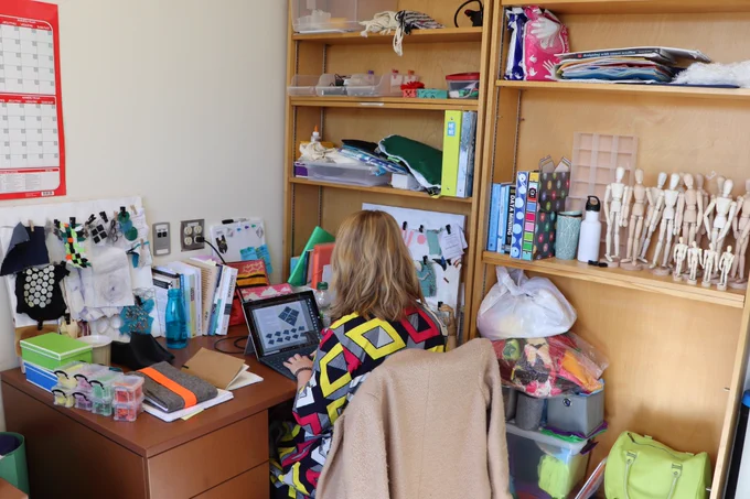 Student working at a computer on a desk surrounded by crafting materials and mini mannequins.