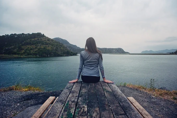 A woman sits alone at the end of a dock, facing out toward the water.