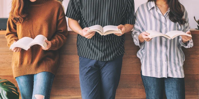 Three people pictured leaning against a wall holding books open