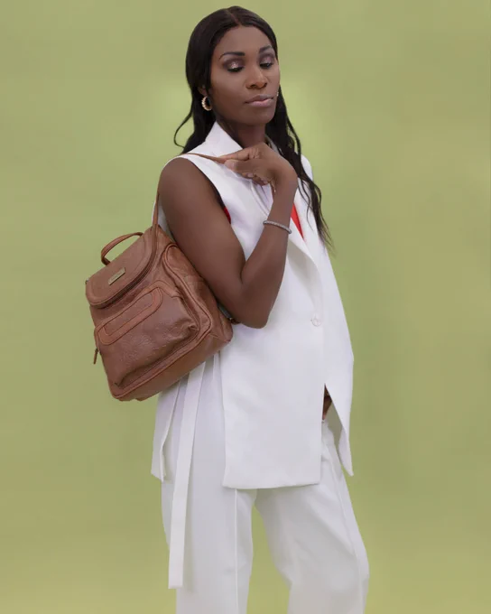 A woman in white pants and a white top slings her hazelnut major backpack over her shoulder as she's ready to take on the work week.