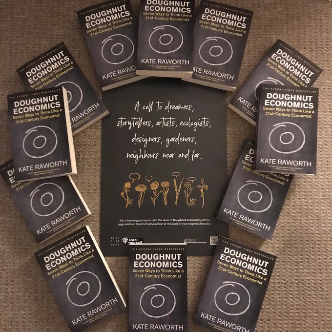 Photo of 12 Doughnut Economics books around a grey poster with white writing, and yellow illustrations of flowers.