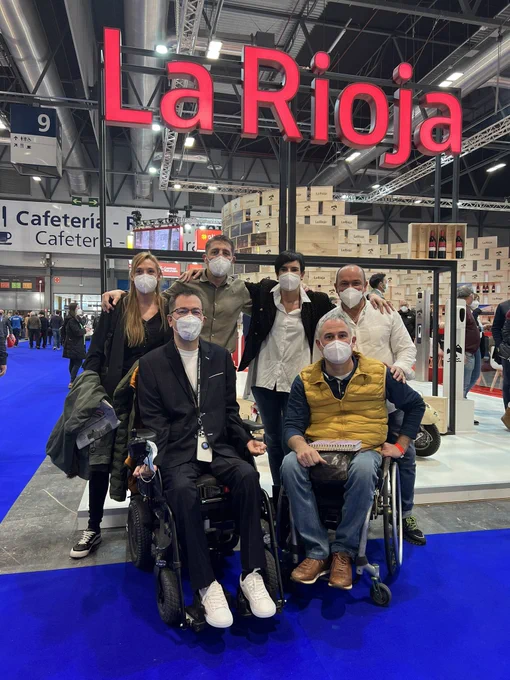 Grupo de 6 personas, 2 de ellas usuarios de silla de ruedas posan en el stand de La Rioja en FITUR