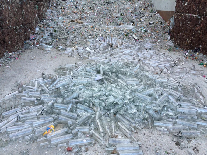 A recycling depot area with a giant pile of intact and broken clear glass bottles