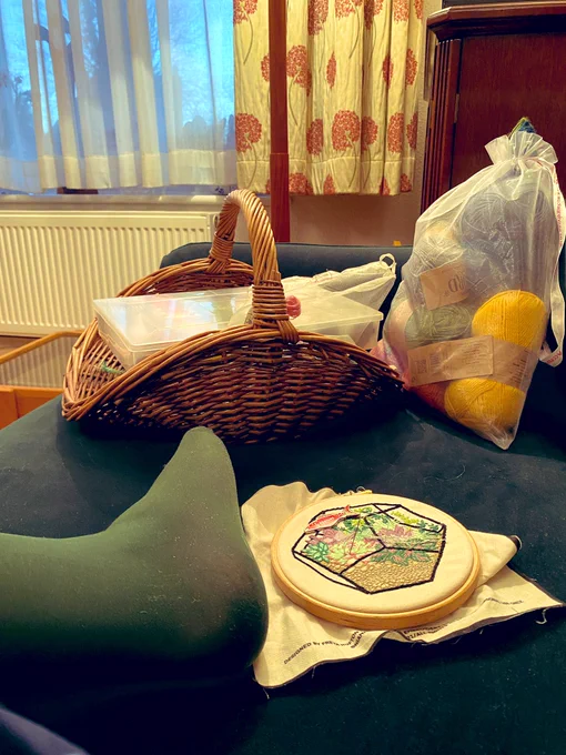 Craft supplies, including knitting and an embroidery project. On a sofa with a foot in shot.