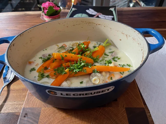 Blue casserole pot with veal casserole garnished with carrots and parsley.