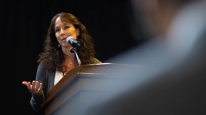 Photo of Dr. Cipolla speaking into a microphone at a lectern in UVM's Hoehl Gallery.