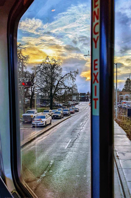 An emergency exit window from inside of a train showing traffic waiting outside and  beautiful pre sunset cloud colors. Emergency exit window is an analogy for non-academic job search.
