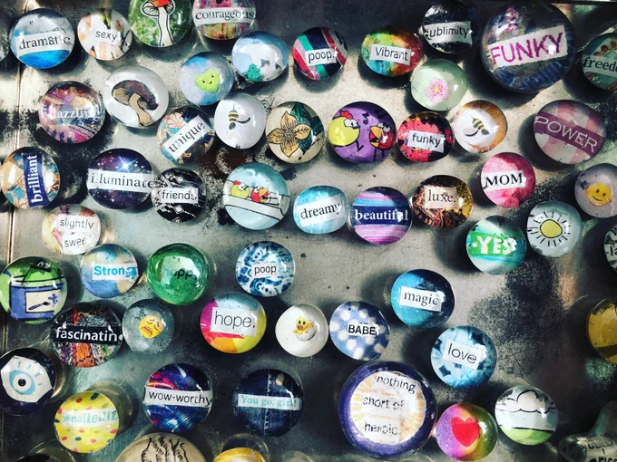 An assortment of glass cabochon fridge magnets with a variety of collage designs on a vintage tin background.