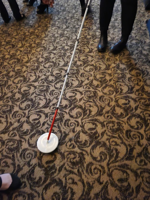 At the O&M booth in the exhibition area of the Dining in the Dark event, a student demonstrates a Dakota Disc cane tip