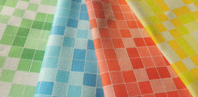Four fabrics from the far left is a green coloured mosaic pattern, then blue mosaic pattern, red mosaic pattern and finally yellow mosaic pattern. Each mosaic pattern features different shades of their respective colour. Mosaic squares are separated by white lines.