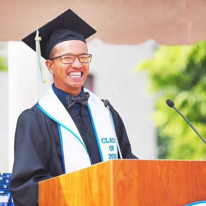 Patton Vo, wearing a black graduation cap and gown, stands at a podium