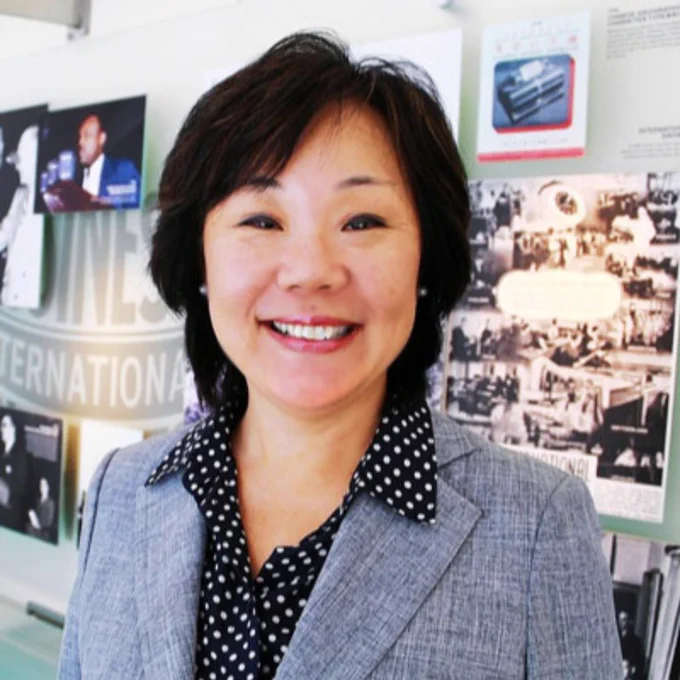 Woman with short black hair in polka dot blouse and gray blazer smiling