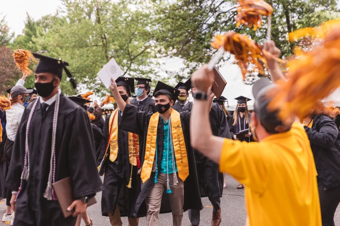 Students walking through a crowd of celebrations in their commencement regalia. 