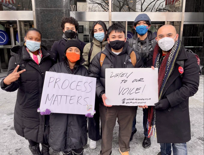 Rose holds up a peace sign with 6 other advocates who hold signs reading: "Process matters" and "Listen to our voice!"