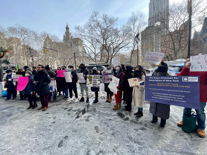 A dozen  advocates gather in a snowy City Hall Park with signs. 