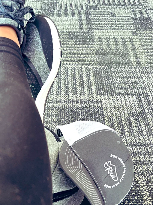 Someone’s legs crossed on a backpack with a hat in the corner. Checkered carpet in the background.