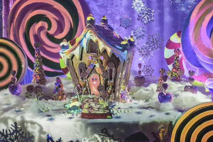 A model gingerbread house, made to look multi-coloured by Lightform technology. Surrounded by sweet statues and giant lollipop swirls in the background.