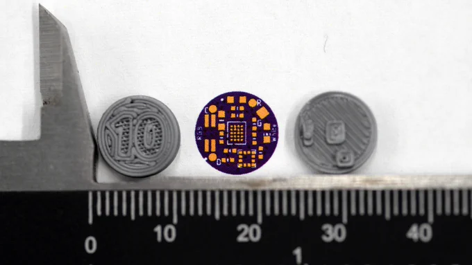 Photo: the rendering printed out at actual size, next to a 3D printed example of a 10mm coin cell and the design itself.