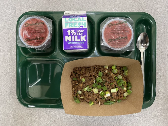A school lunch tray holds a serving of Korean beef, strawberry fruit cups, and milk.