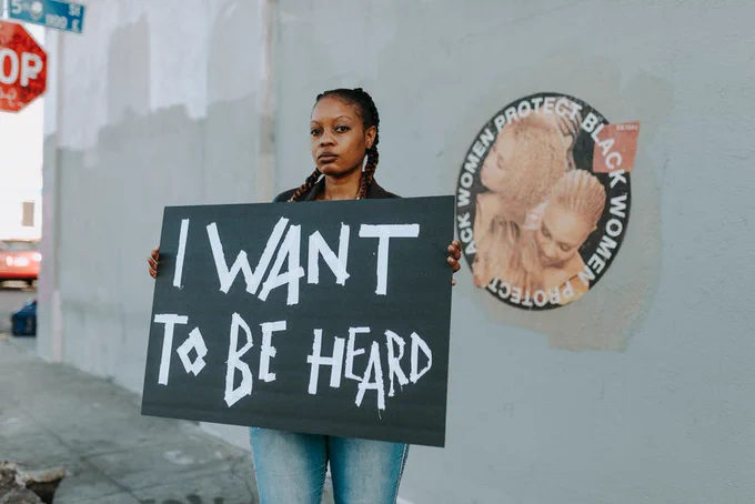 brown adult holds sign that reads, "I want to be heard."