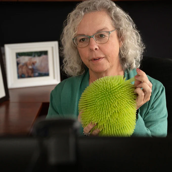 Lu Randall is a light-curly haired female facing the camera while holding a sensory ball.