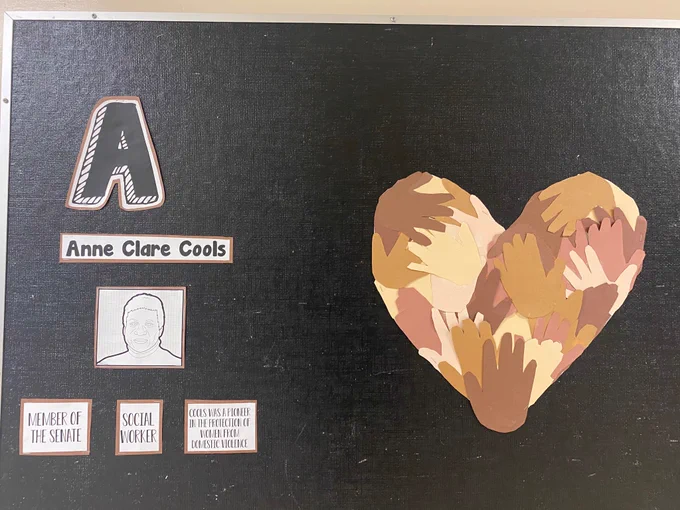Bulletin board with a description of Anne Clare Cools and a heart of multicultural hands. 