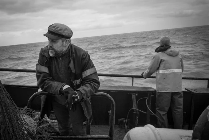 Two men standing at the edge of a fishing boat, the wild North Sea behind them.