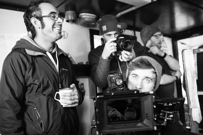 A group of men setting up camera equipment. One smiling with a hot drink in his hand.