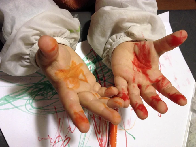 A child's hands, covered in yellow and red pen