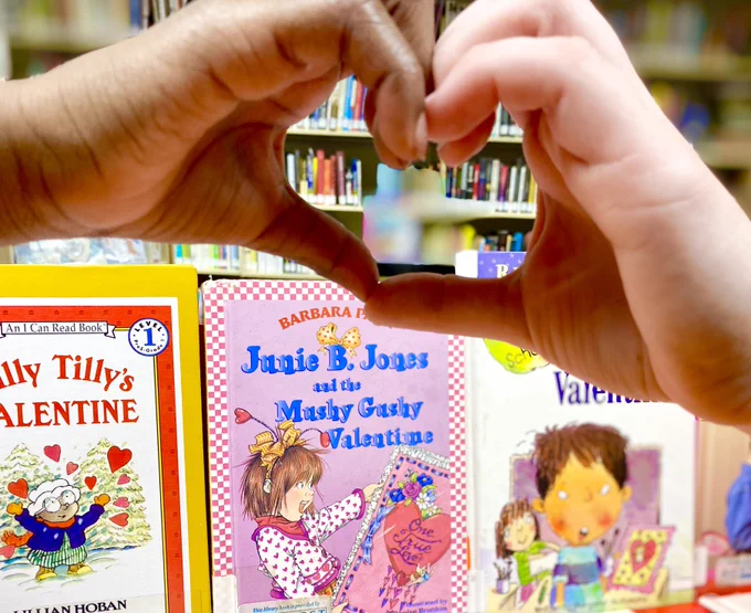 a childs' hand and adult's hand make a heart shape in front of children's Valentine themed books