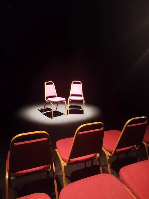 2 chairs in a spotlight on a theatre stage 