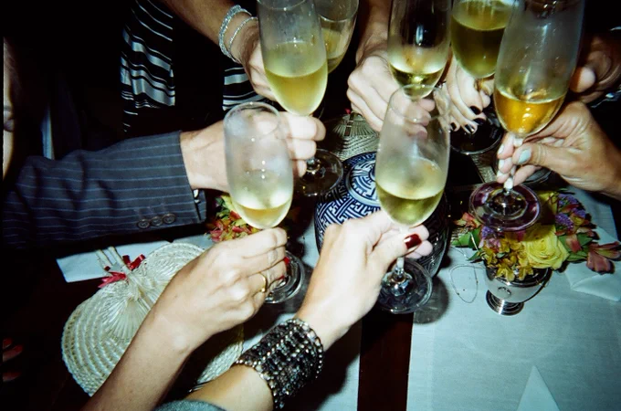 Seis mãos brindando com taças de champanhe frente a uma mesa florida.