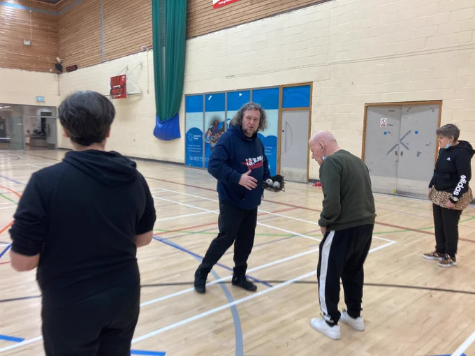 VI baseball coach wearing a glove demonstrating to three participants in a sports hall