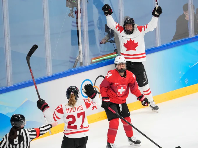 Two Team Canada hockey players celebrate a goal while a Swiss player stands in between them 